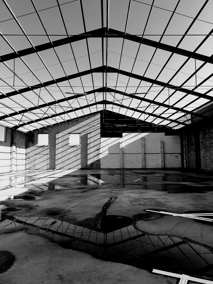 who-we-are Black and white photograph of an empty industrial warehouse with geometric shadows.