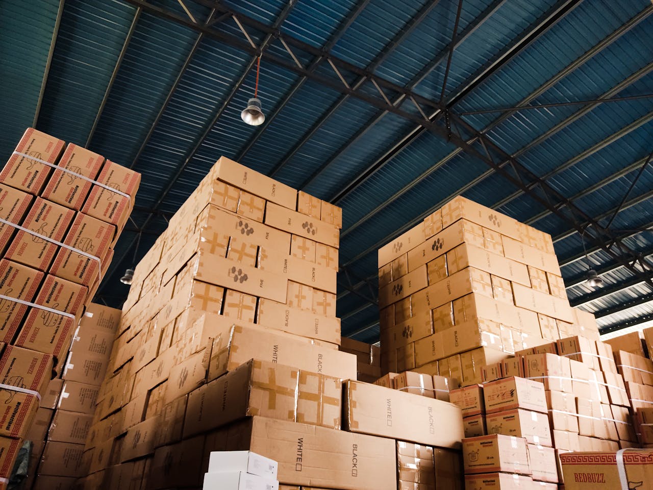 services-01 High stacks of cardboard boxes organized in a warehouse with a blue metal ceiling.